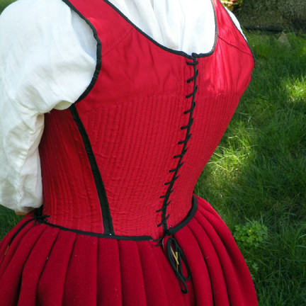 This petticoat laced closed at the back. The pleats are knife pleats, with a layer of wool pleated in with the outer fabric. The waistband is bound around the raw edges of the pleats.